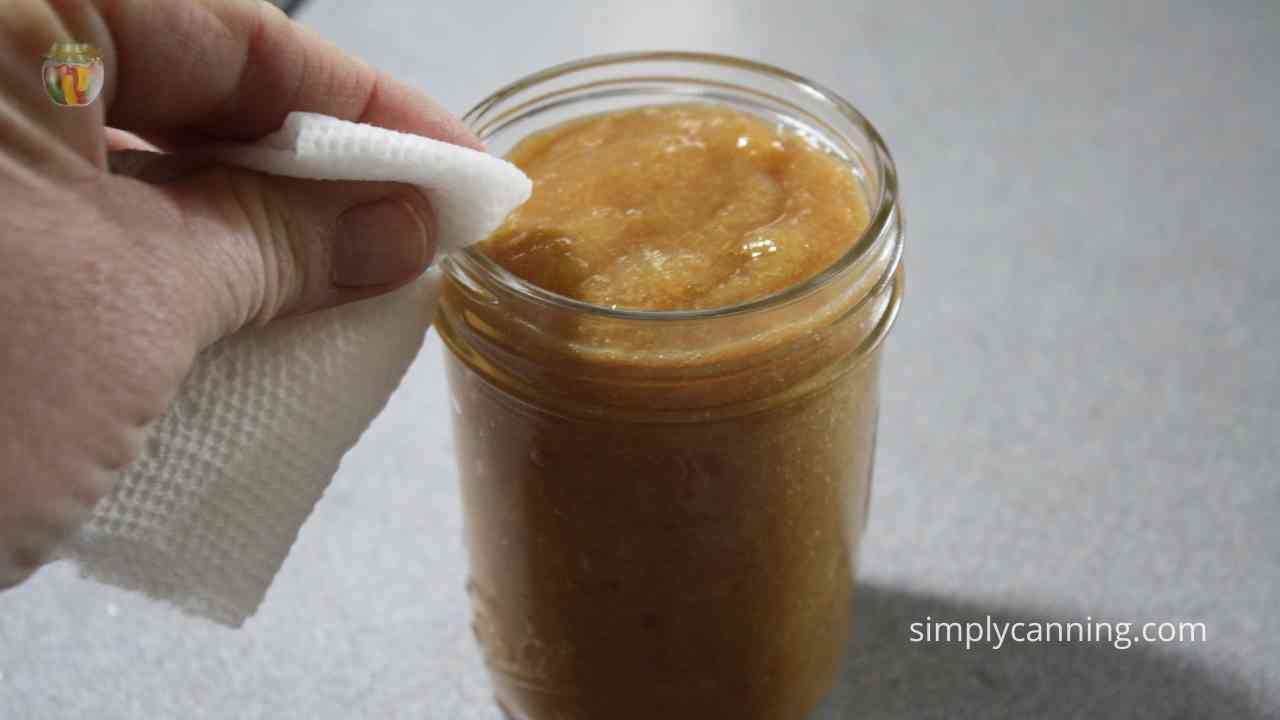 Wiping rim of a jar of apple butter with a wet paper towel.