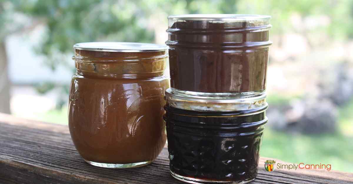 Three small jars of various fruit butters sitting on a railing outdoors.