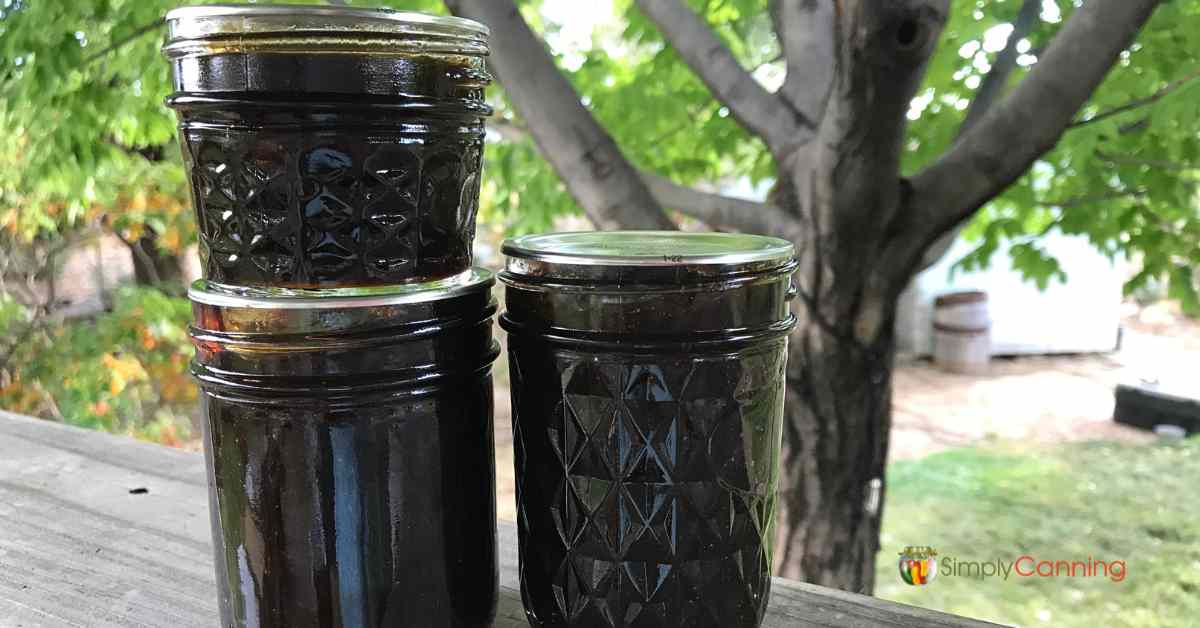 Three jars of deeply colored plum butters sitting on a ledge outdoors.