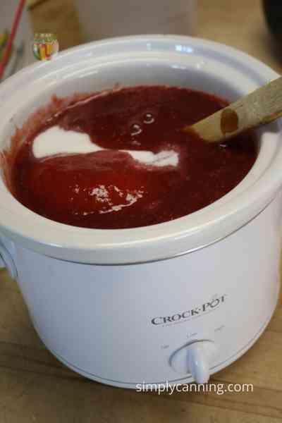 Stirring sugar into the slow cooker full of plum pulp.