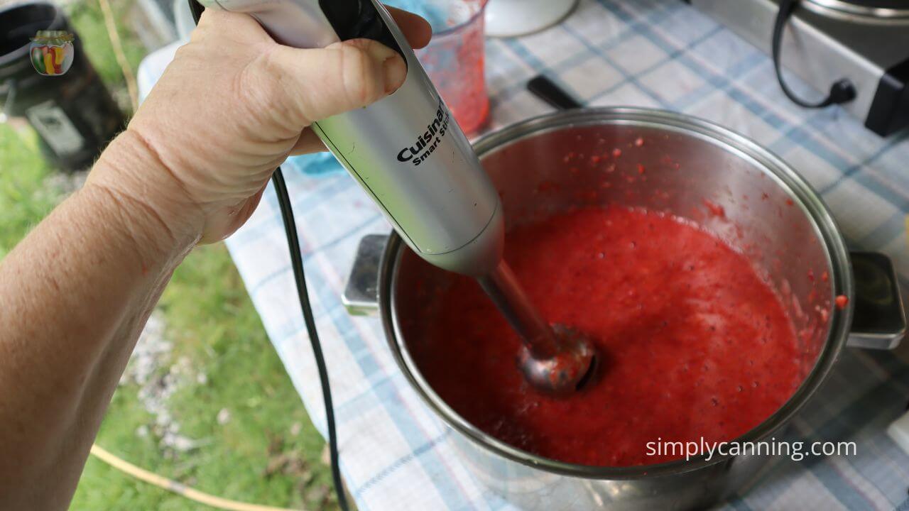 Pot with strawberries being pureed by a stick blender