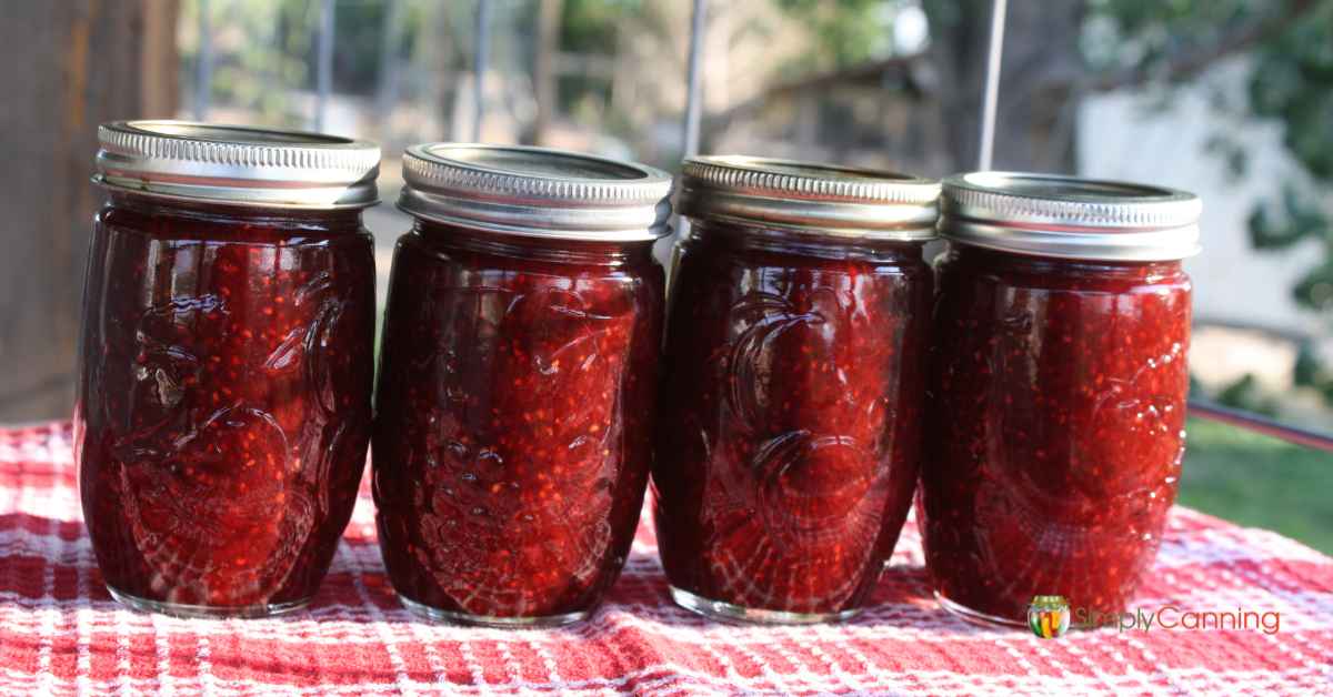 4 jars of homemade mixed berry jam sitting on a red and white checked dish cloth.  